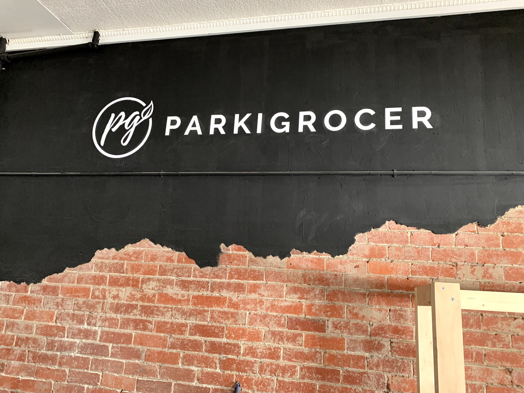 red brick wall with black shop signage saying PARKIGROCER in white font.